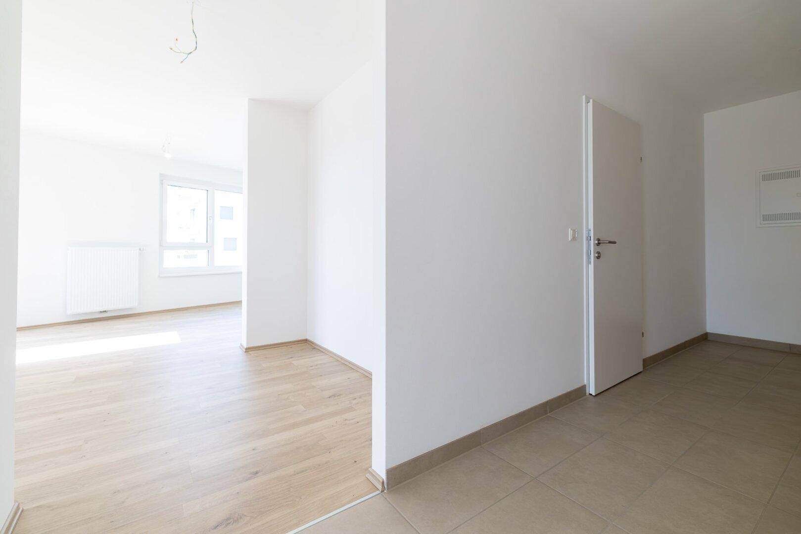 Heller Flur mit Übergang von Fliesen- zu Laminatboden, der zu weiteren Räumen führt.