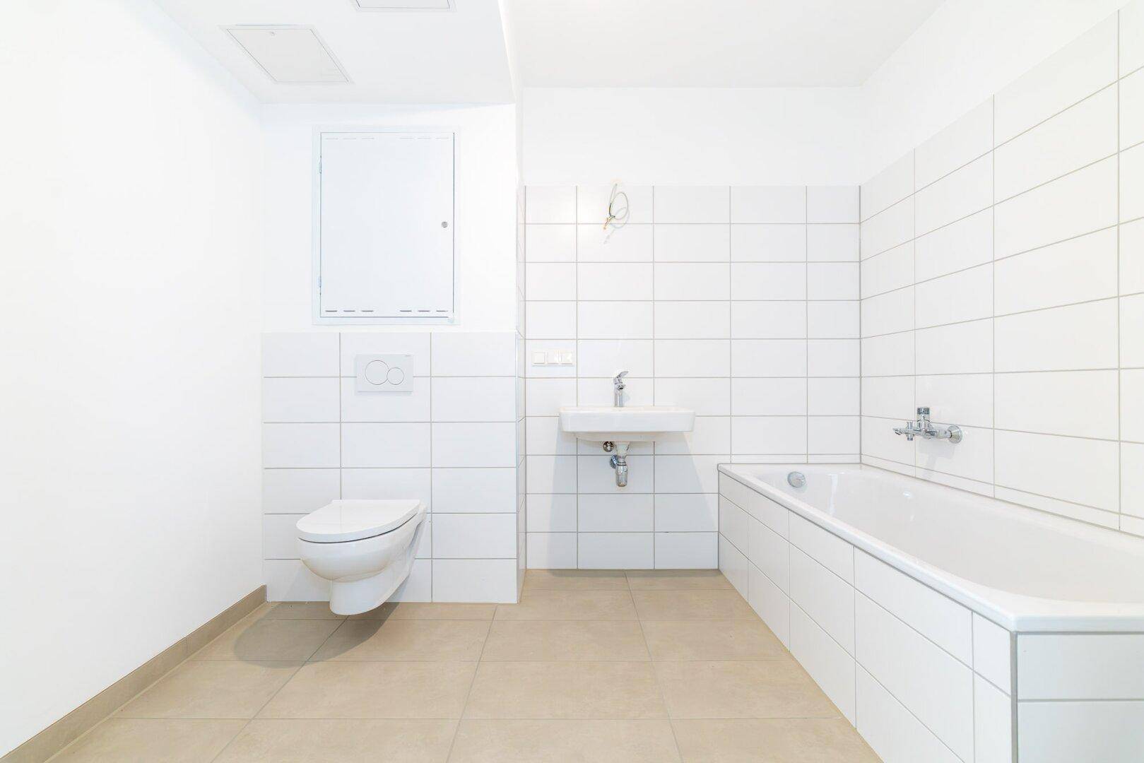 Sauberes Badezimmer mit weißen Wandfliesen und beigefarbenem Boden, ausgestattet mit Badewanne und WC.