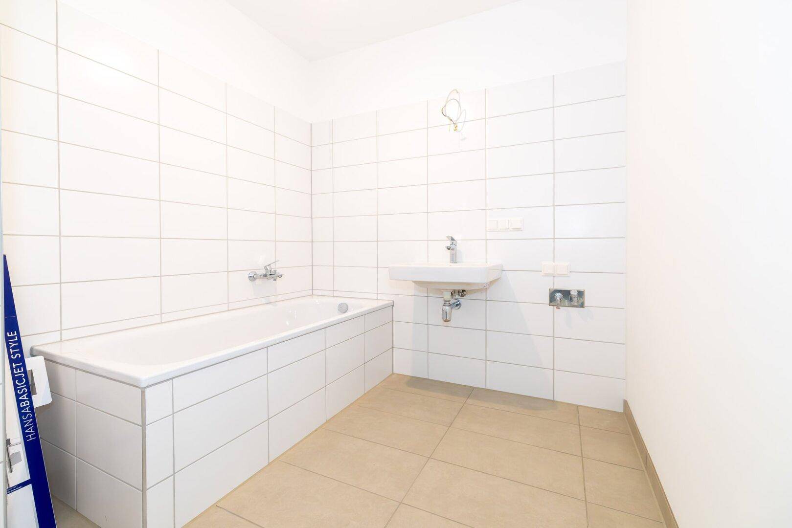 Modernes Badezimmer mit weißen Fliesen, Badewanne und Waschbecken, bereit zur Nutzung.