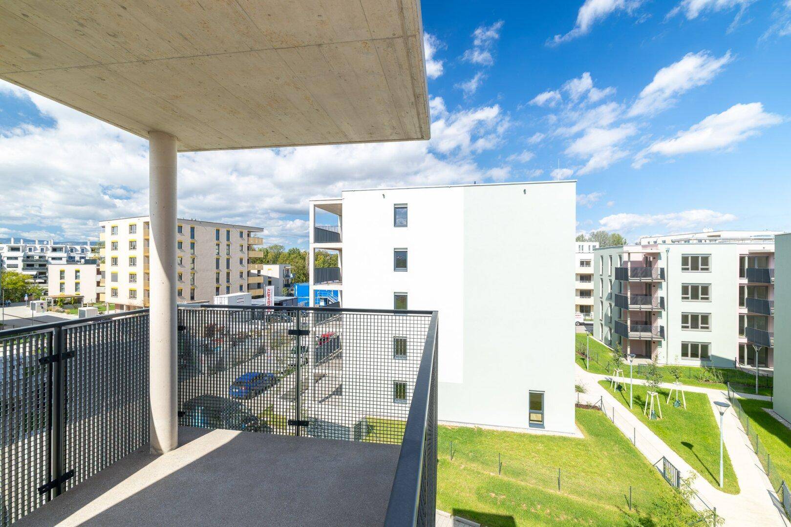 Moderner Balkon mit Betonüberdachung und Gittergeländer, bietet Blick auf die Wohnanlage.