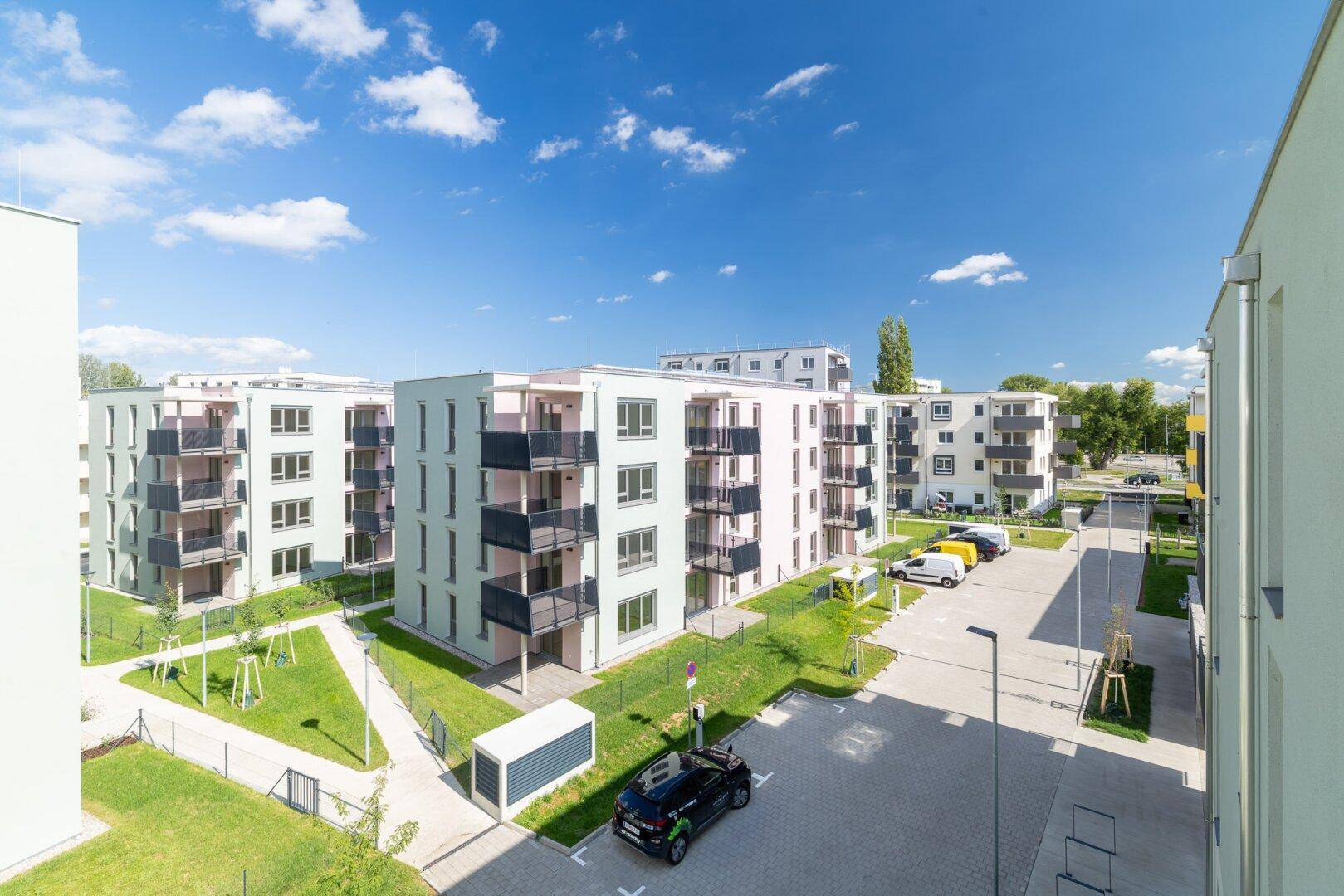 Weitläufige Wohnanlage mit modernen Mehrfamilienhäusern, Parkplätzen und gepflegten Grünflächen.