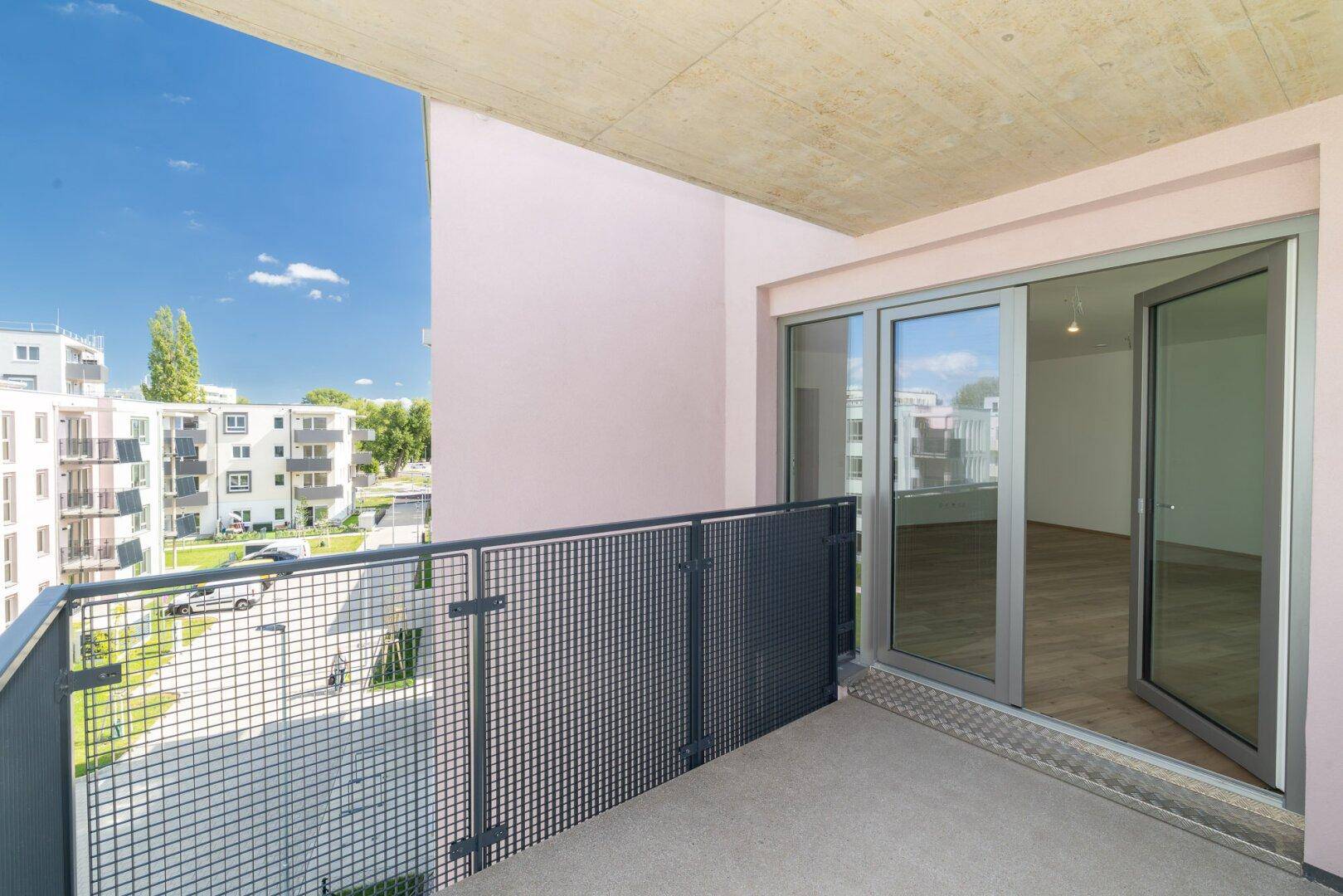 Heller Balkon mit Blick auf die Wohnanlage und Zugang zu einem modernen Innenraum.