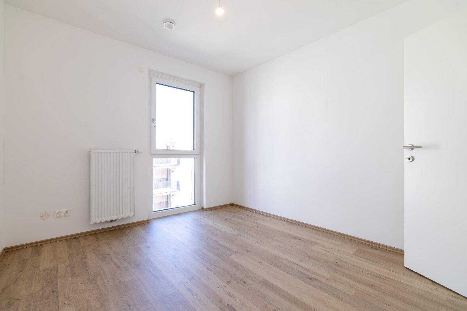 Lichtdurchflutetes Schlafzimmer mit Laminatboden und großem Fenster, bietet viel Helligkeit.