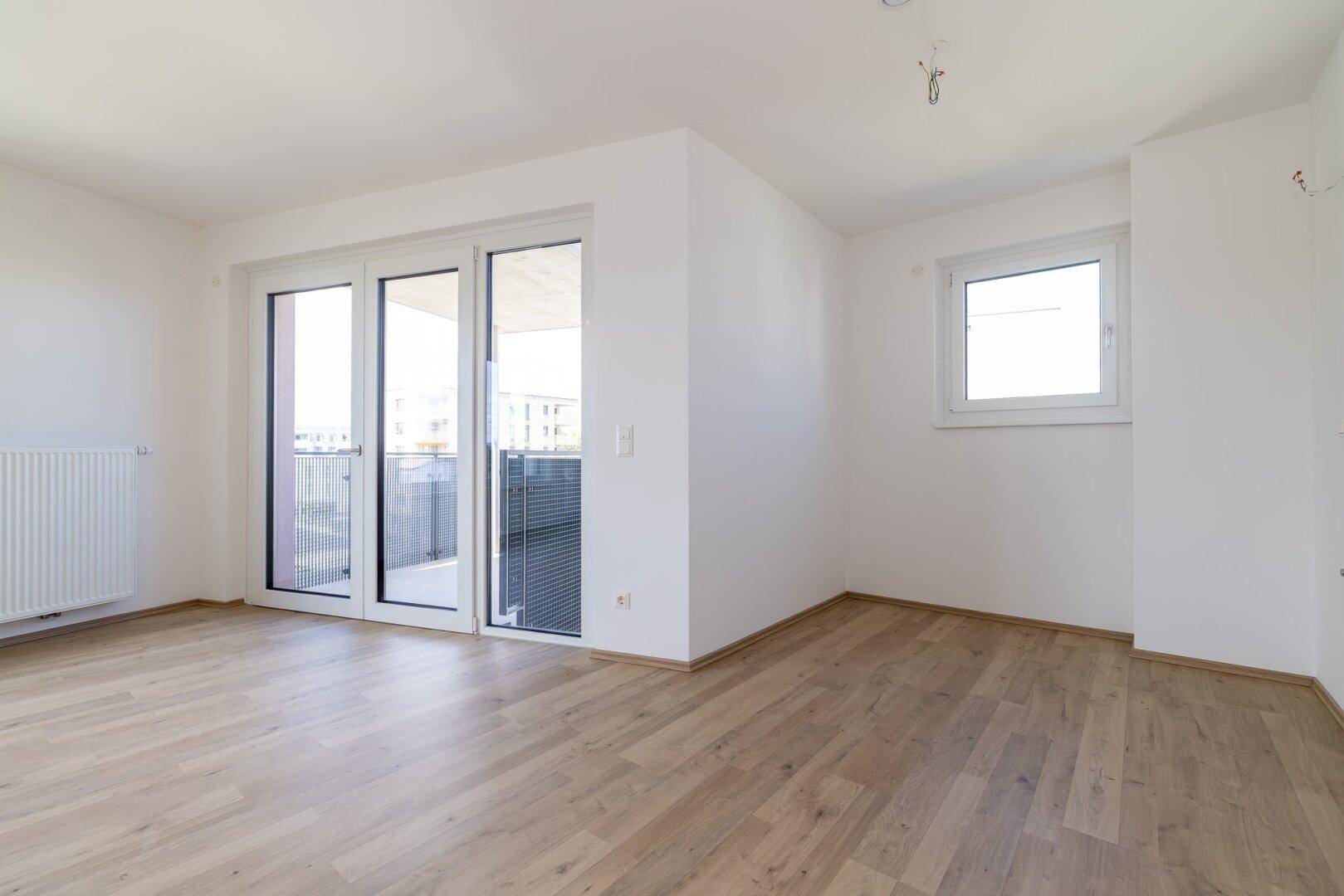Helles Wohnzimmer mit Laminatboden, Fenster und Balkontür, ideal für viel Tageslicht.