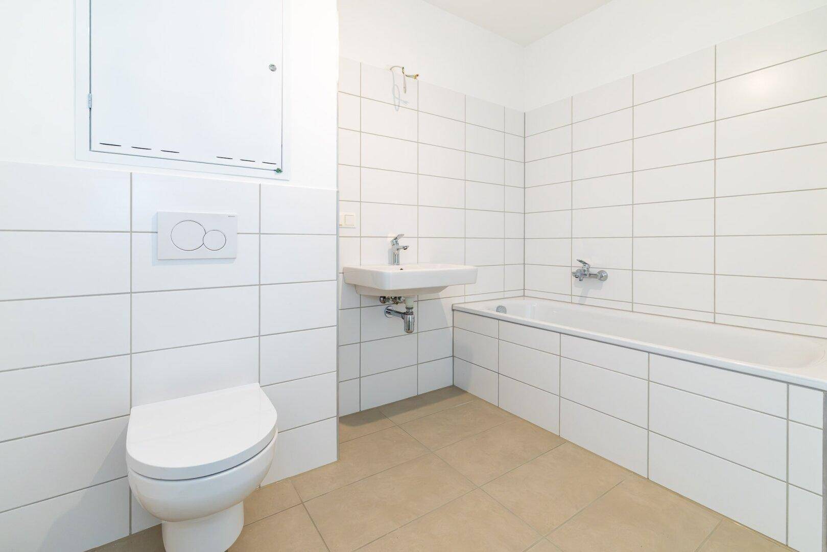 Modernes Badezimmer mit weißen Wandfliesen, beigen Bodenfliesen, Badewanne und WC.