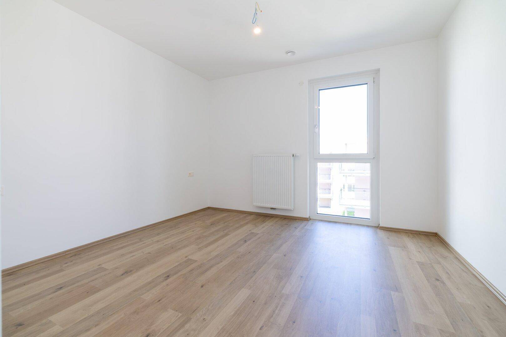 Helles Schlafzimmer mit Laminatboden, weißen Wänden und einem großen Fenster.