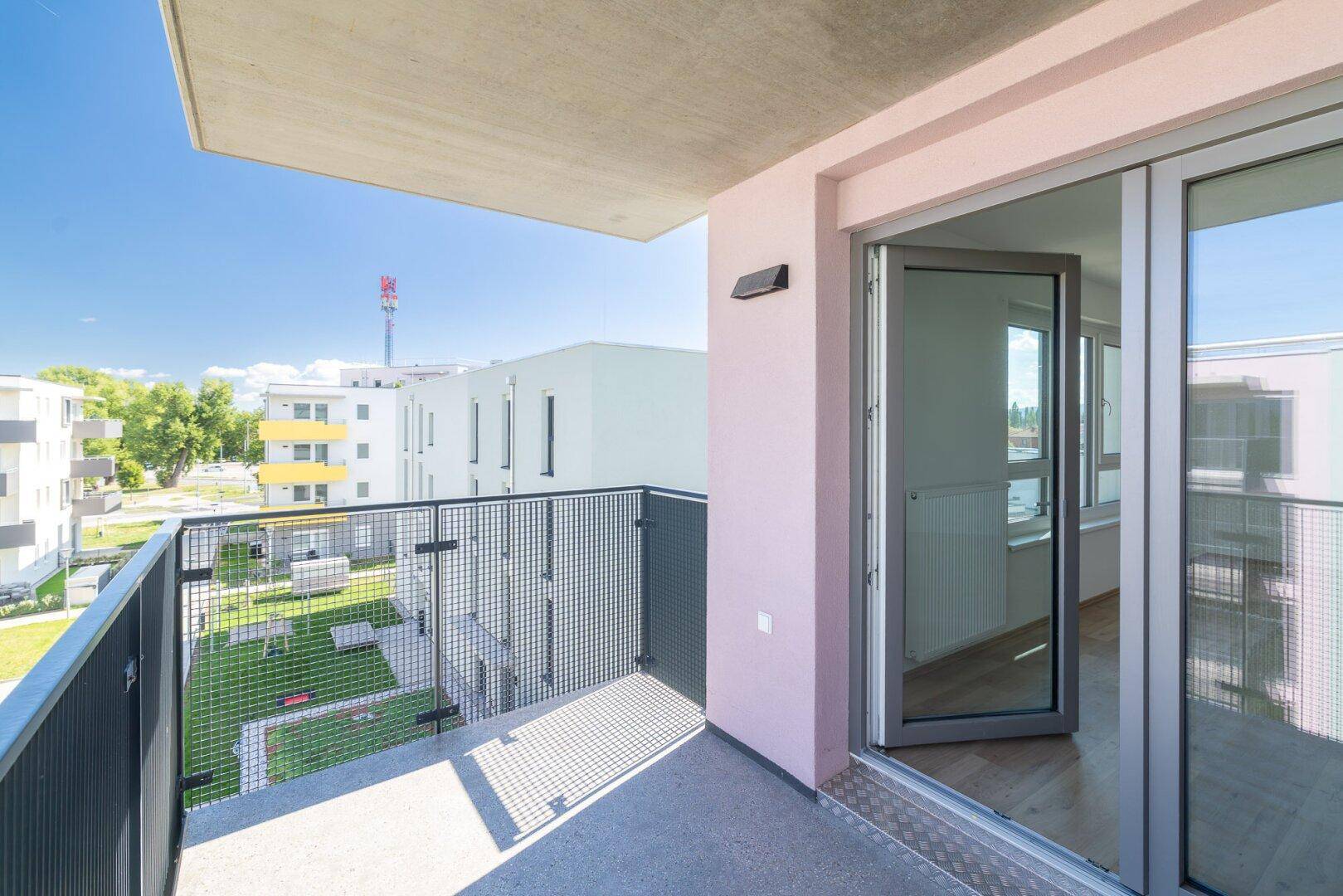 Balkon mit Zugang zum Innenraum und Blick auf die moderne Wohnanlage und Grünflächen.