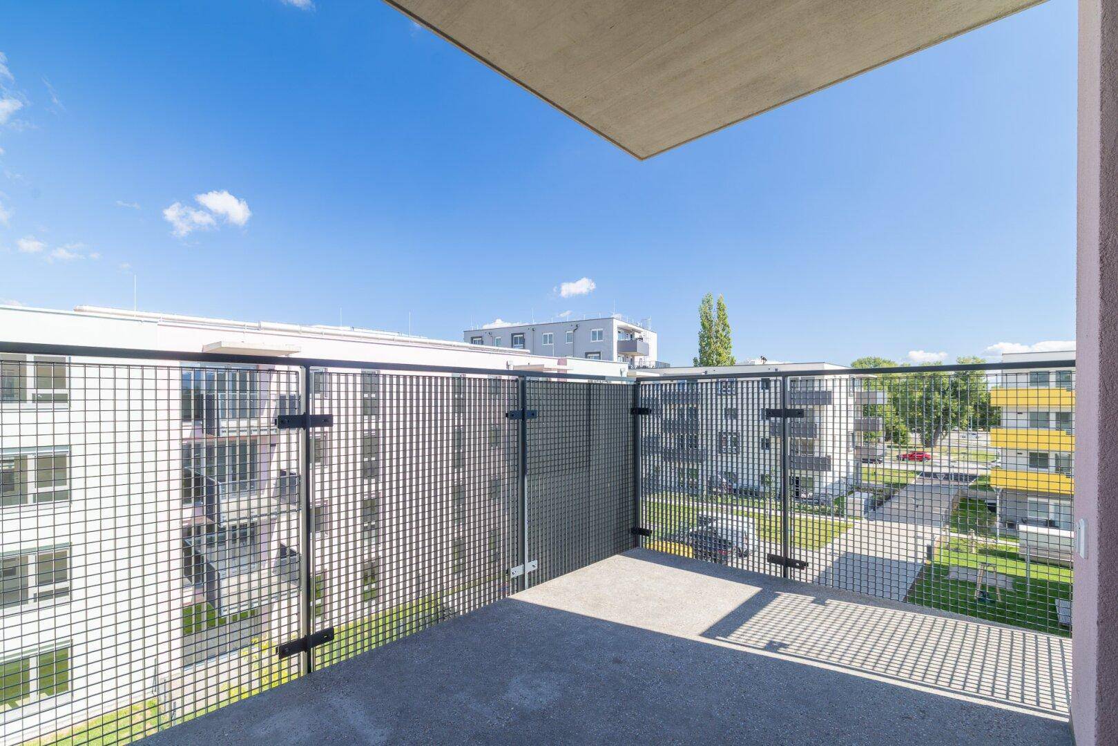 Heller Balkon mit Gittergeländer und Blick auf die umliegenden Neubauten und Grünflächen.