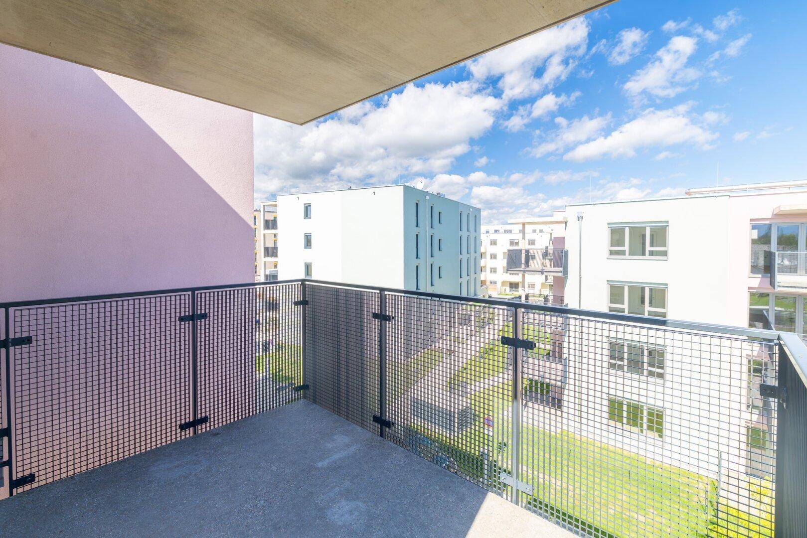 Sonniger Balkon mit weitem Blick über die moderne Wohnanlage und den blauen Himmel.