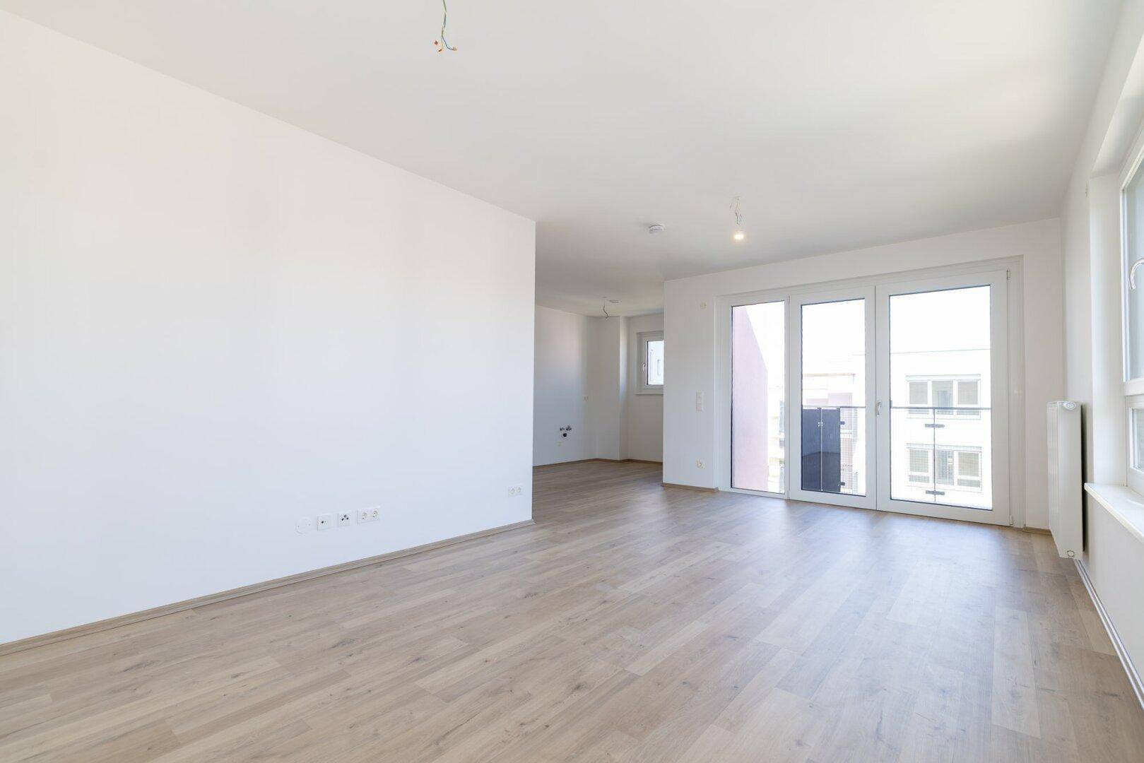 Geräumiges, helles Zimmer mit Laminatboden, großen Fenstern und Zugang zum Balkon.