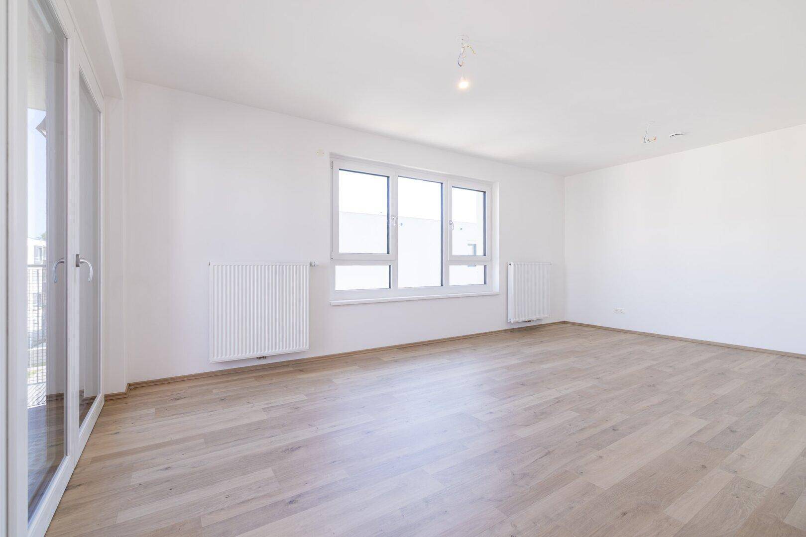 Helles und geräumiges Zimmer mit großen Fenstern, Laminatboden und Heizkörpern.