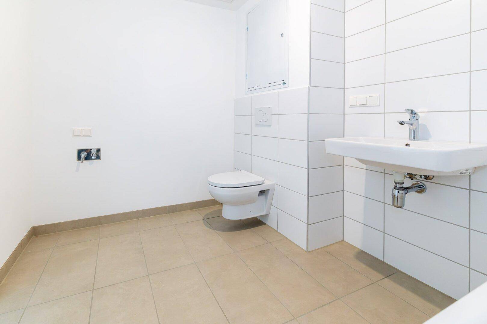 Modernes Badezimmer mit weißen Wandfliesen, beigen Bodenfliesen und wandhängendem WC.