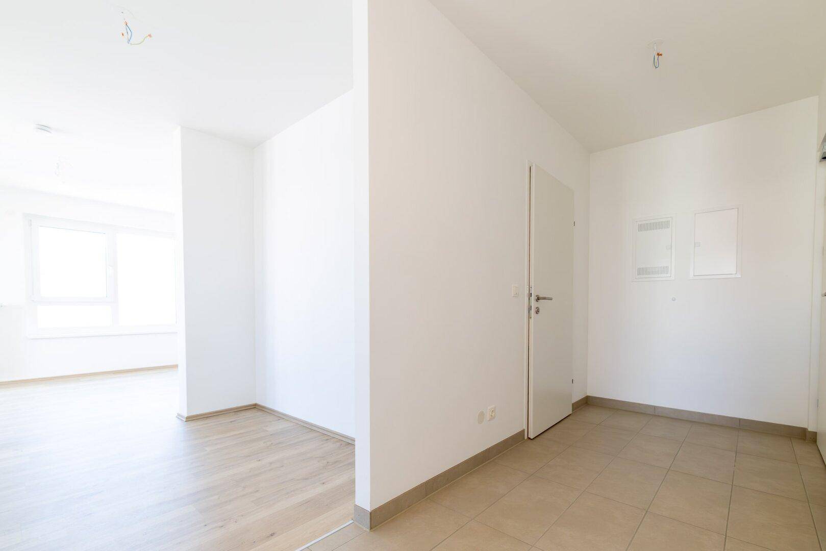 Heller Eingangsbereich mit beigen Fliesen und offenem Übergang zu einem Zimmer mit Laminatboden.