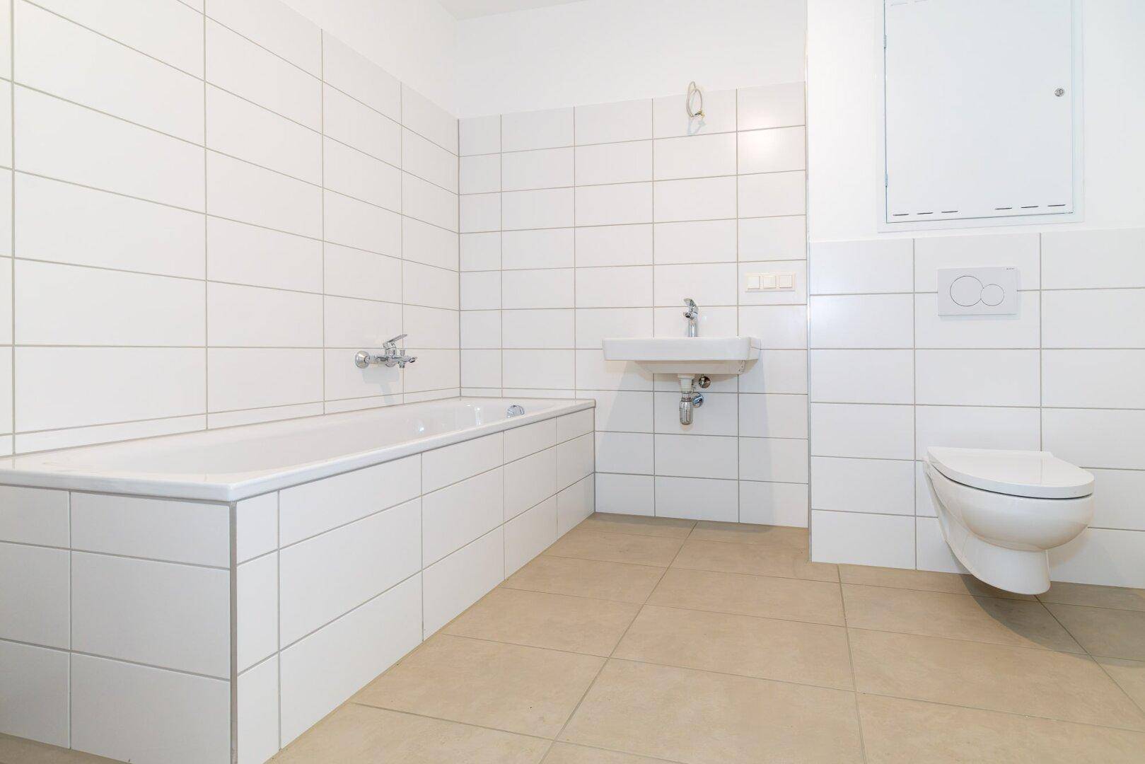 Modernes Badezimmer mit weißen Fliesen, Badewanne, wandhängendem WC und Waschbecken.