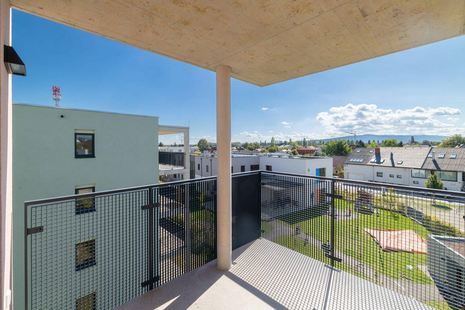 Moderner Balkon mit Betonüberdachung und Metallgeländer, bietet Blick auf Grünflächen und Berge.