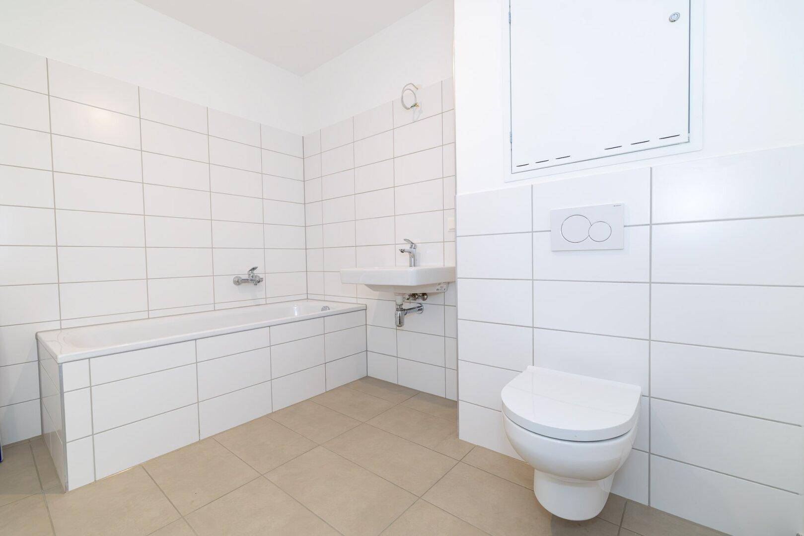 Helles Badezimmer mit Badewanne, wandhängendem WC und Waschbecken, komplett gefliest.