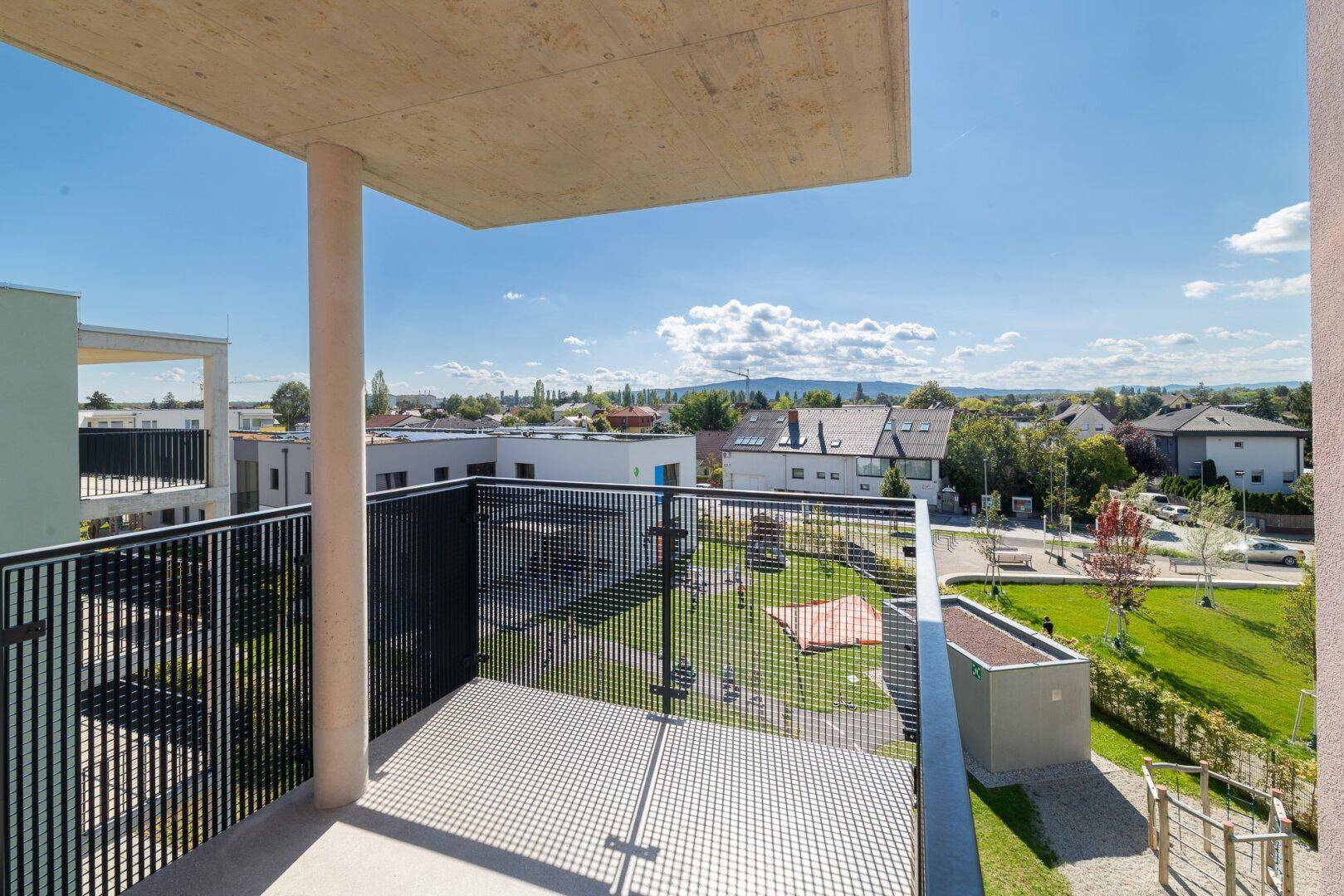 Heller Balkon mit moderner Architektur, Blick auf die Wohnanlage und die umliegende Landschaft.