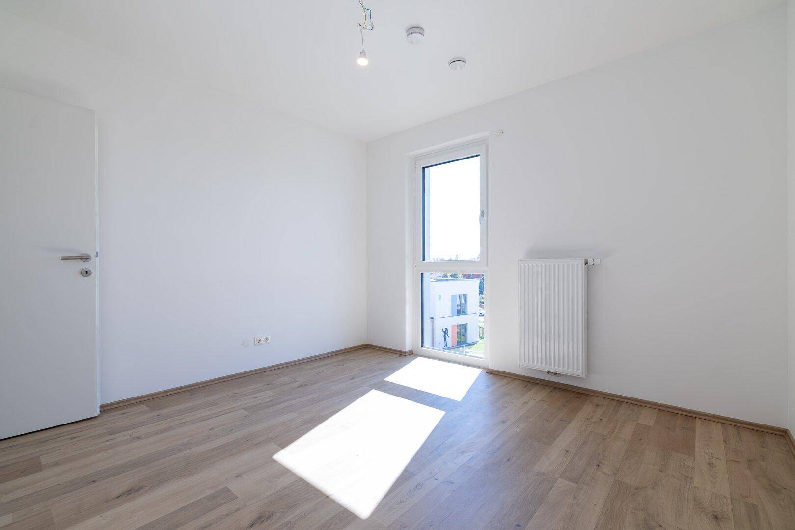 Freundliches Schlafzimmer mit Laminatboden, weiß gestrichenen Wänden und einem Fenster.