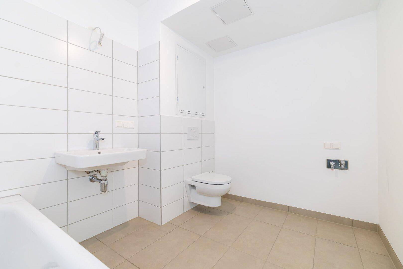 Funktionales Badezimmer mit Waschbecken, wandhängendem WC und Platz für weitere Ausstattung.