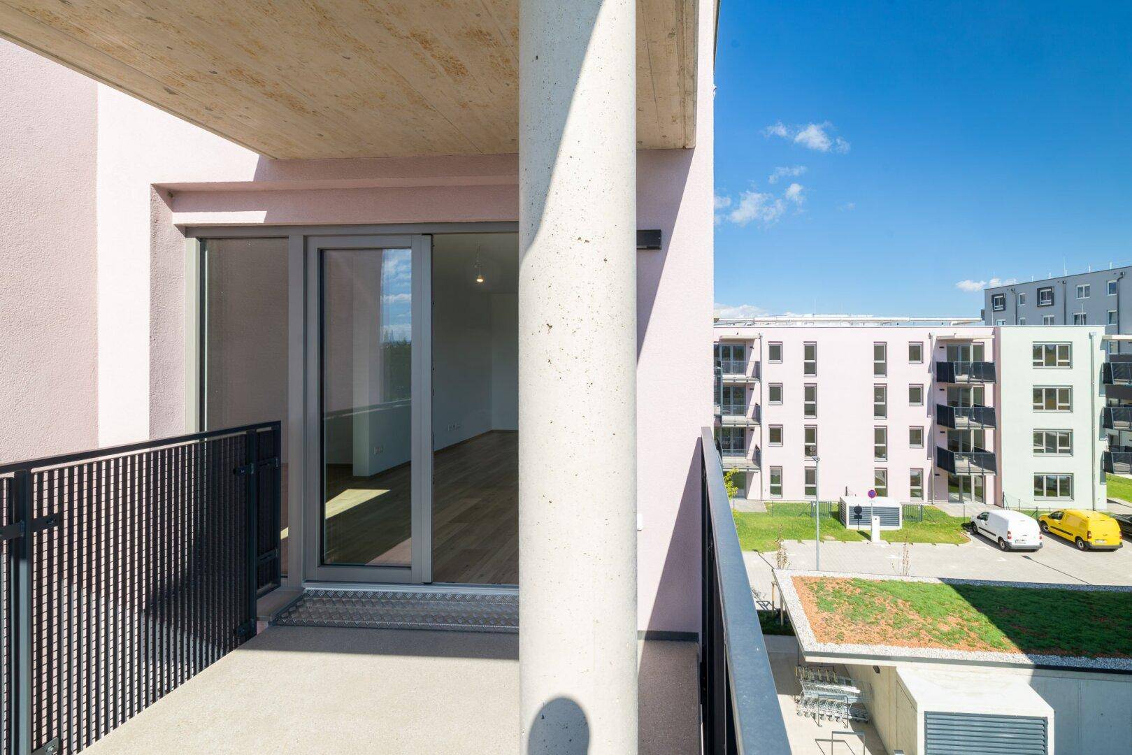 Balkon mit Blick in einen hellen Innenraum und auf die umliegenden Gebäude der Wohnanlage.