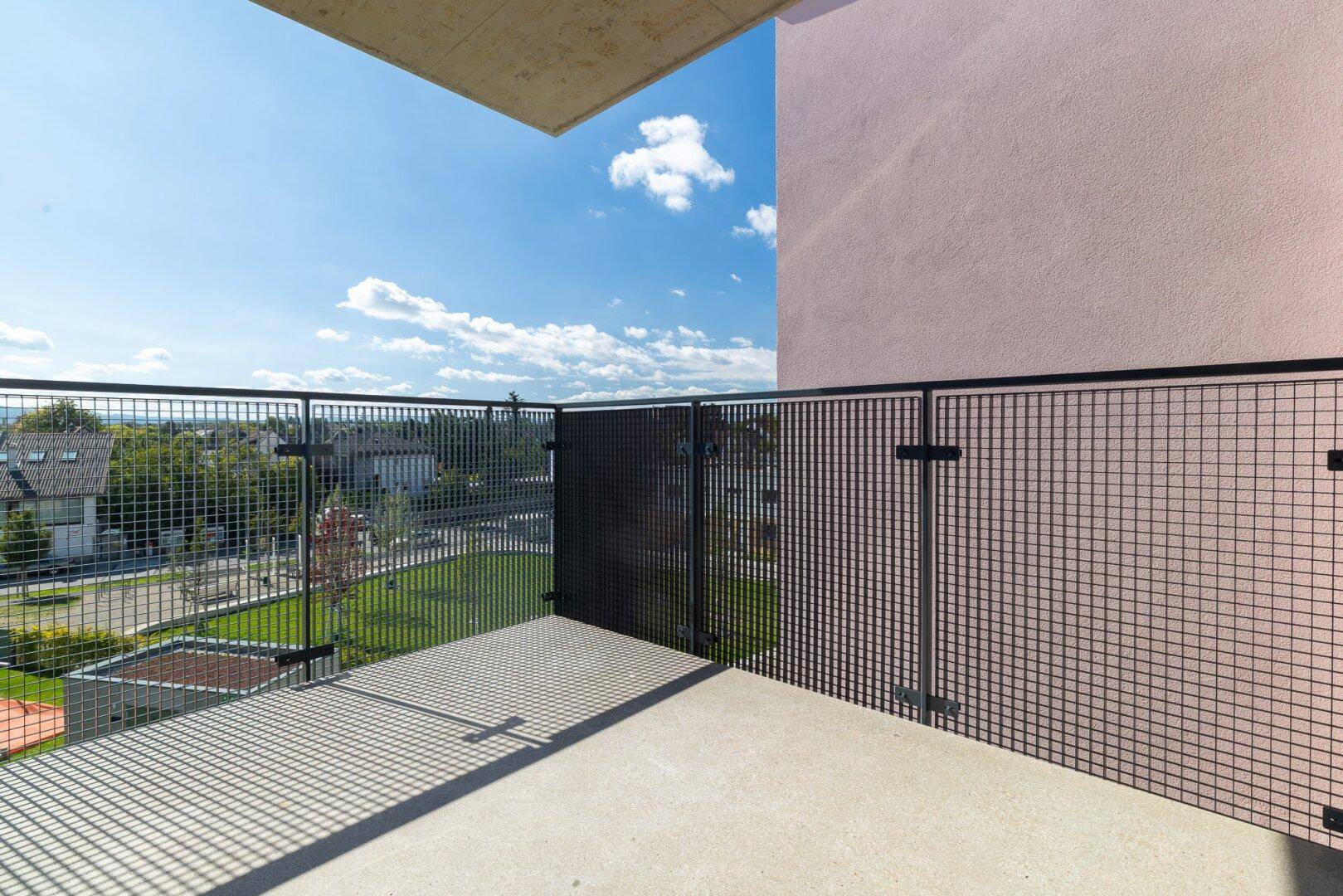 Detailansicht des Balkons mit modernem Metallgittergeländer und Betonboden unter blauem Himmel.