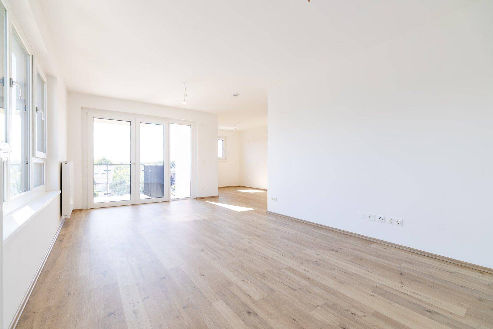 Großzügiger, heller Wohnraum mit Laminatboden, großen Fenstern und Zugang zum Balkon.