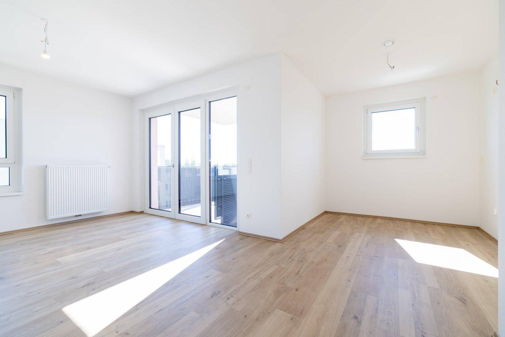 Geräumiges, helles Zimmer mit Laminatboden, einem Fenster und Balkonzugang.