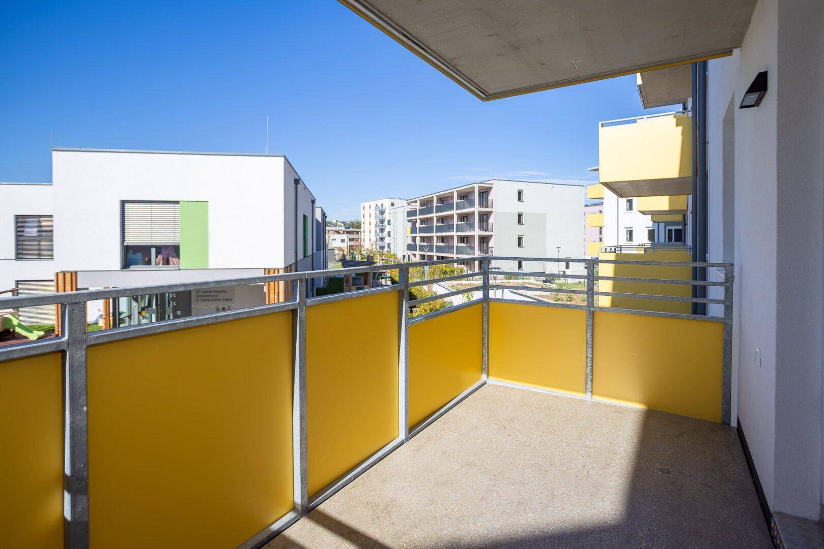 Heller Balkon mit gelber Brüstung und freiem Blick auf die moderne Wohnsiedlung.