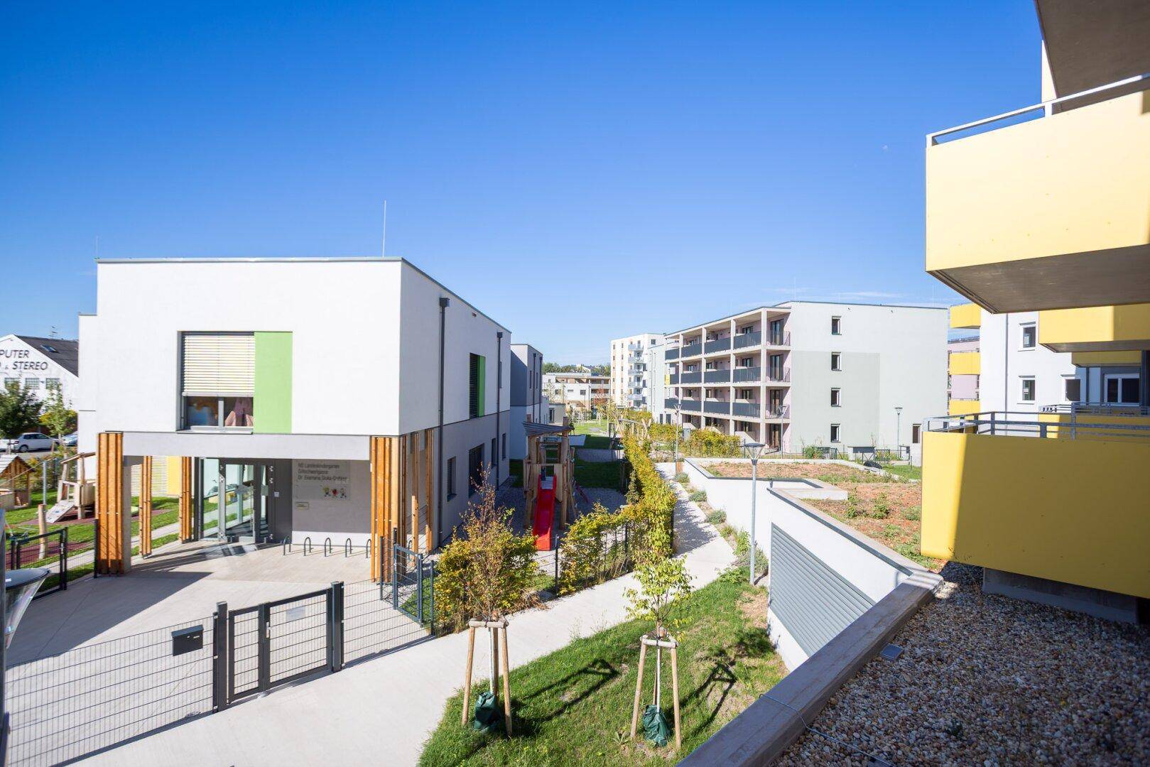 Moderne Architektur eines Gemeinschaftsgebäudes mit Spielplatz und weiteren Wohngebäuden im Hintergrund.