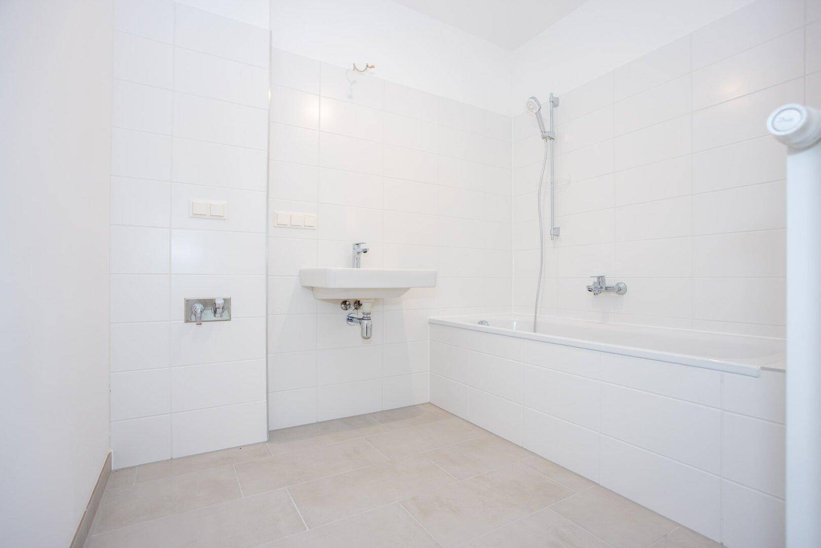 Modernes Badezimmer mit weißen Fliesen, Badewanne und einem einzelnen Waschbecken.