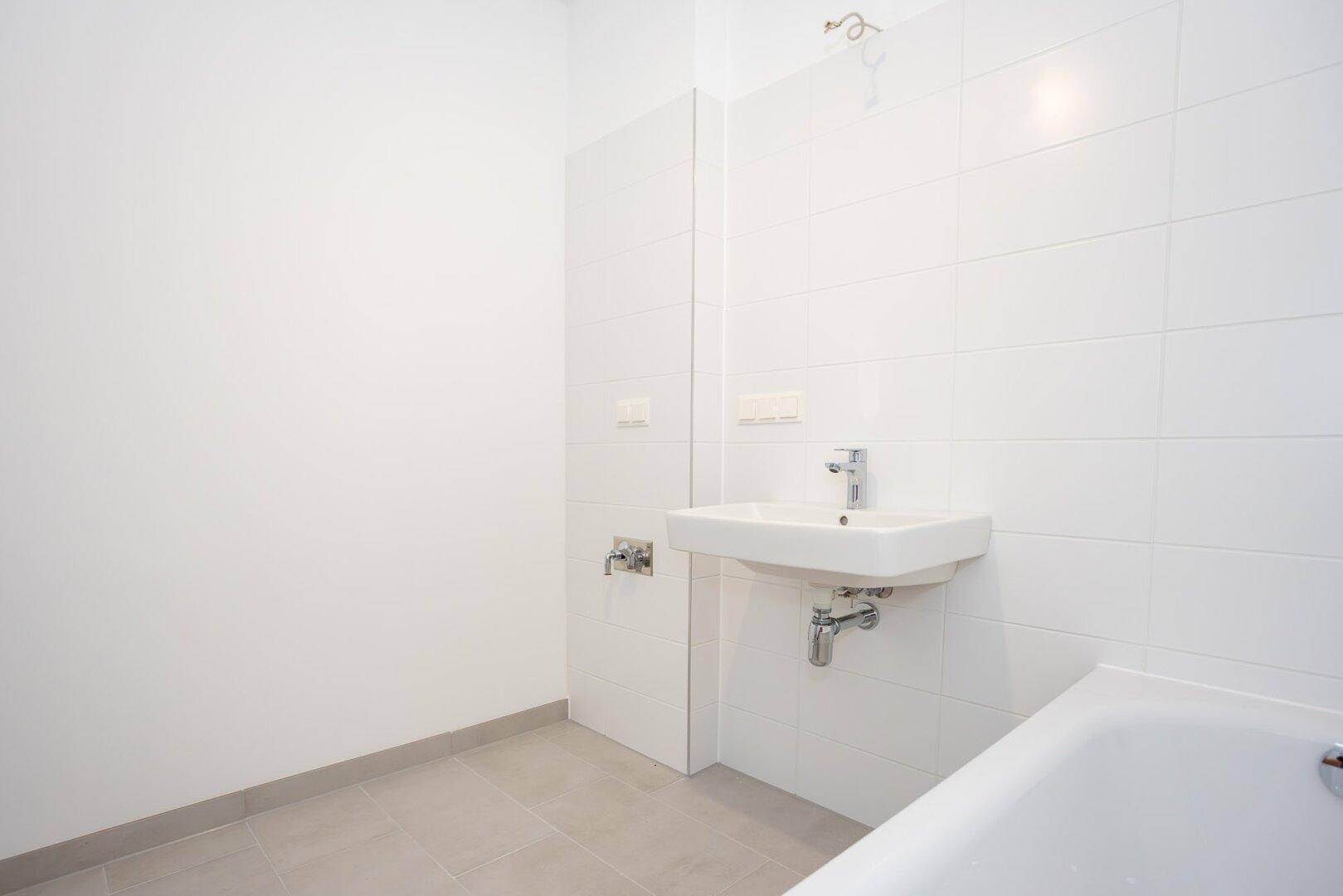 Helles Badezimmer mit weißen Wandfliesen und einem modernen Waschbecken.