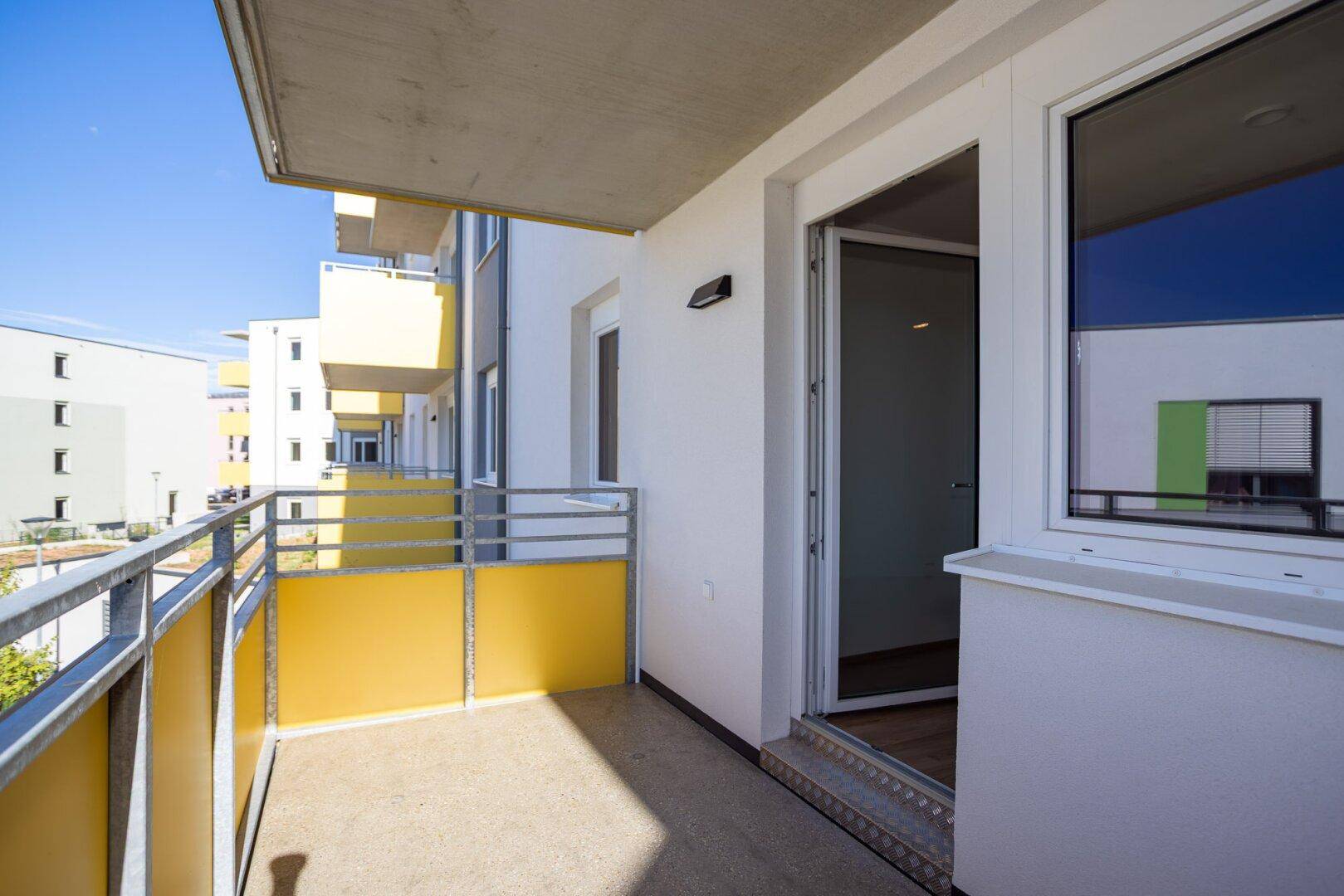 Heller Balkon mit gelber Brüstung und offener Tür, die in den Wohnbereich führt.