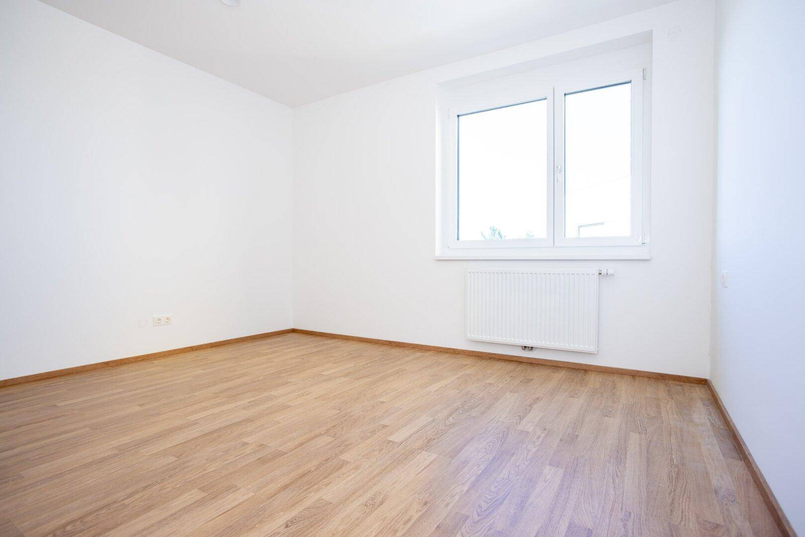 Geräumiges Schlafzimmer mit hellem Laminatboden und einem Fenster, das viel natürliches Licht hereinlässt.