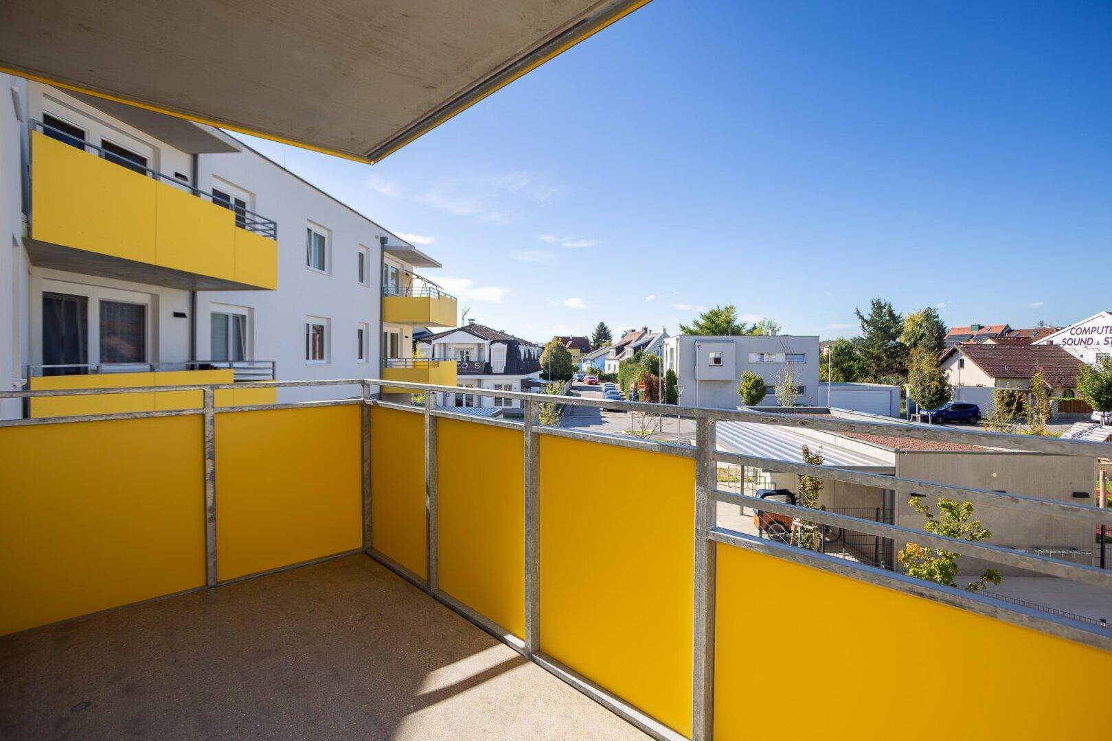 Geräumiger Balkon mit gelber Brüstung und Blick auf die umliegenden modernen Gebäude.