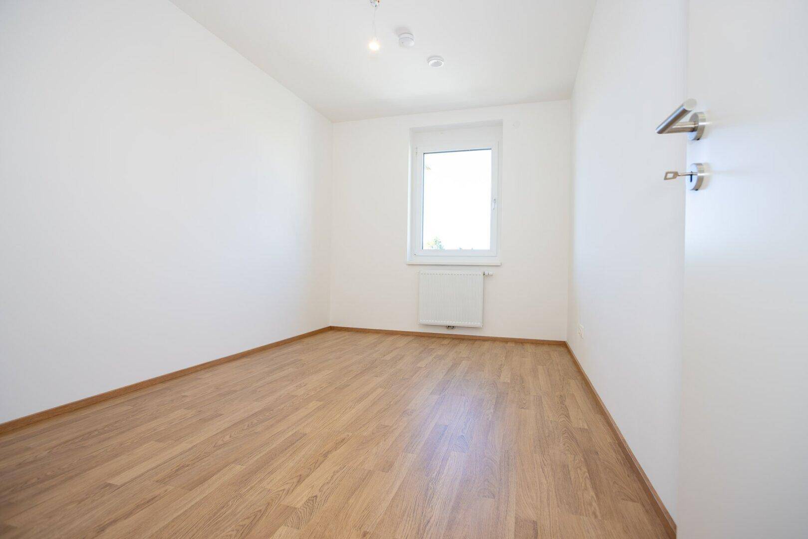 Kleineres, helles Zimmer mit Laminatboden und einem Fenster, ideal als Kinder- oder Arbeitszimmer.