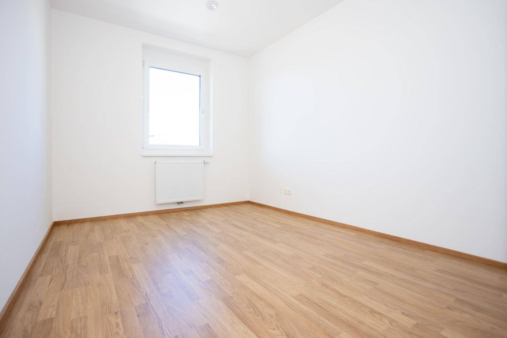 Freundliches Zimmer mit Laminatboden und weißen Wänden, bereit zur individuellen Gestaltung.