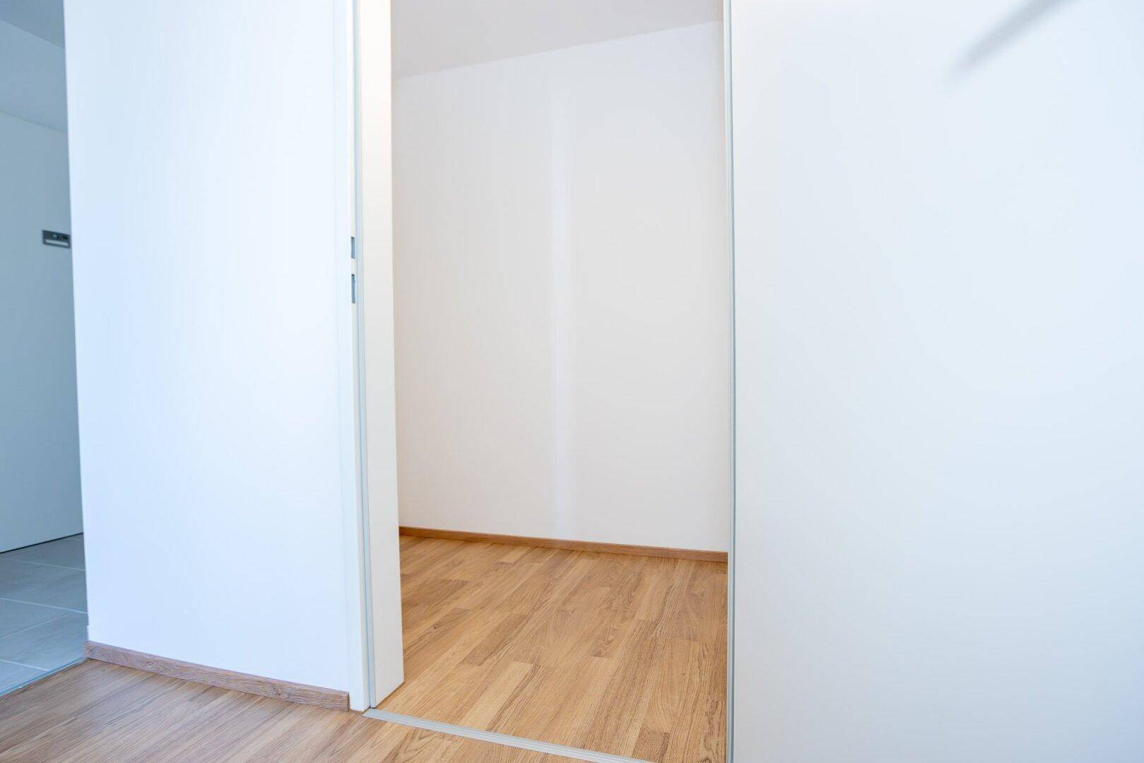 Offener Durchgang von einem gefliesten Flur in ein Zimmer mit Laminatboden.