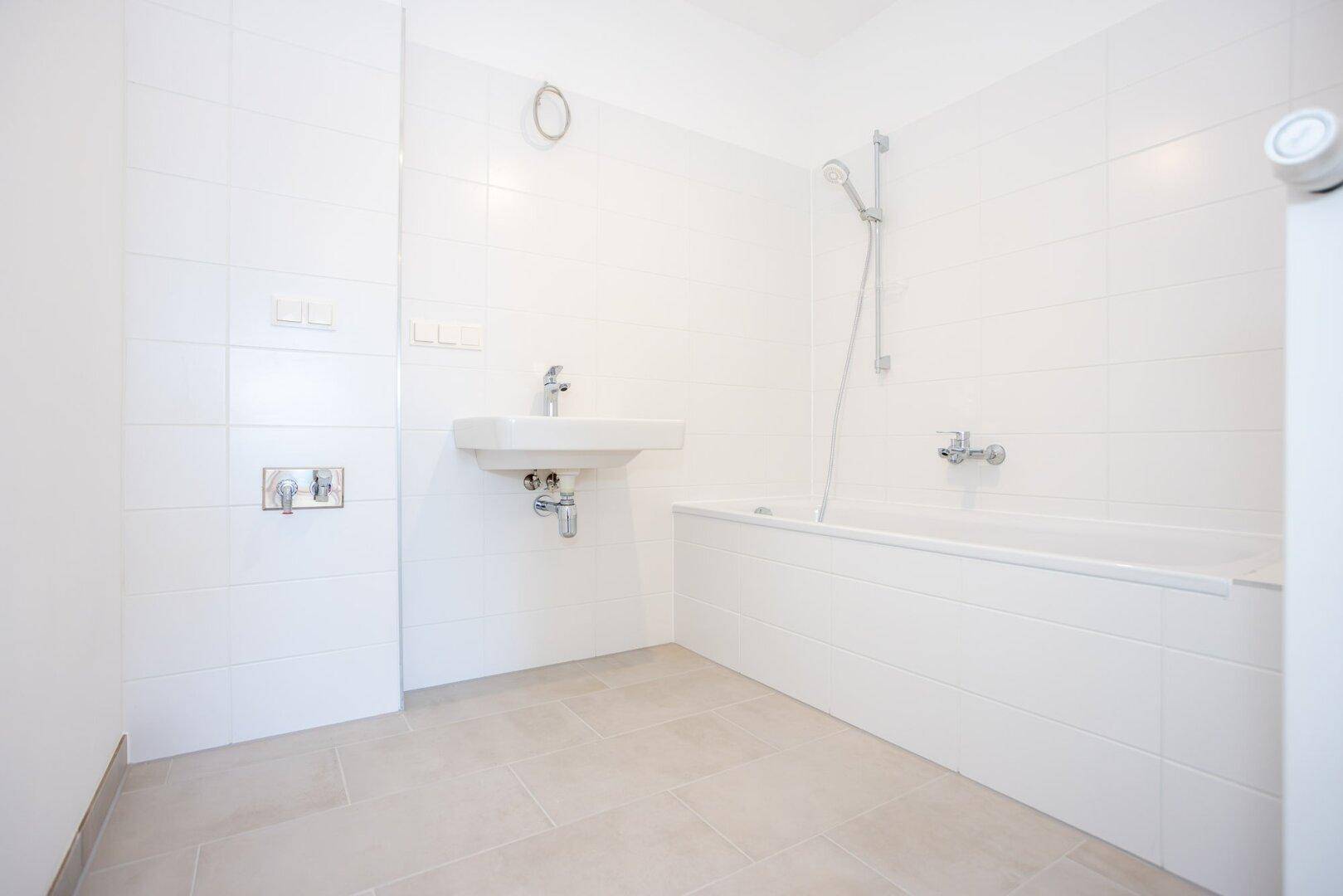Modernes Badezimmer mit weißen Fliesen, Badewanne und Waschbecken, in neuwertigem Zustand.
