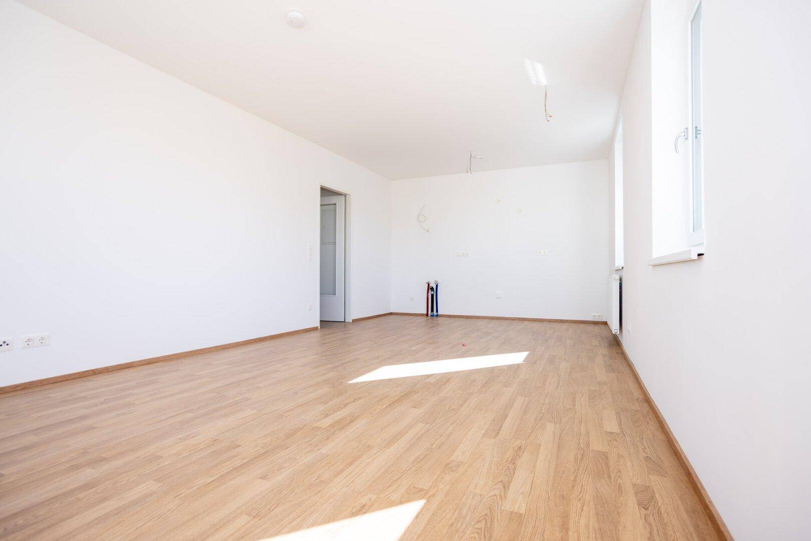 Heller Raum mit Laminatboden und Anschlüssen für eine Küche, bereit für den Einbau.