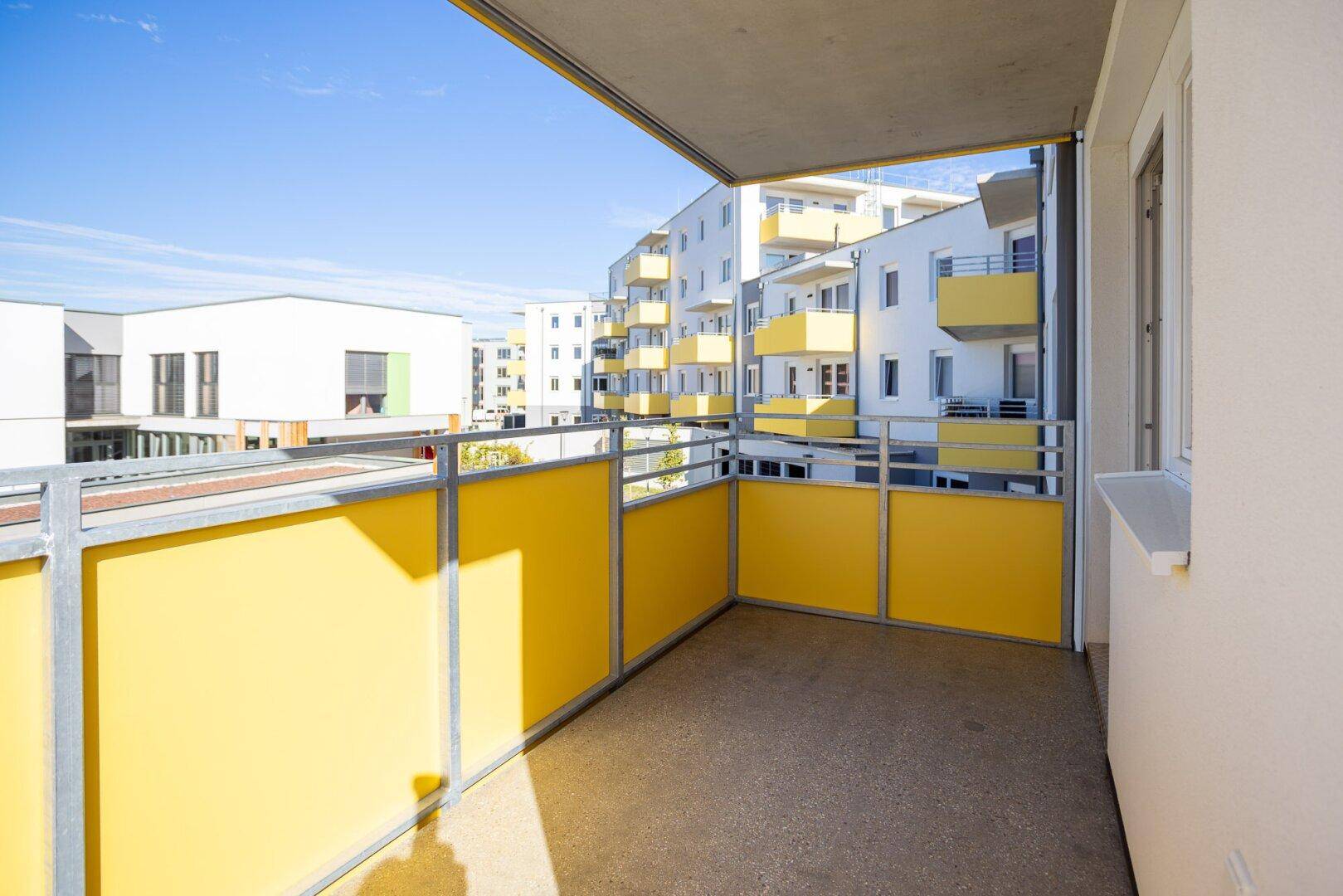 Moderner Balkon mit gelben Akzenten und Ausblick auf die Neubauwohnanlage.