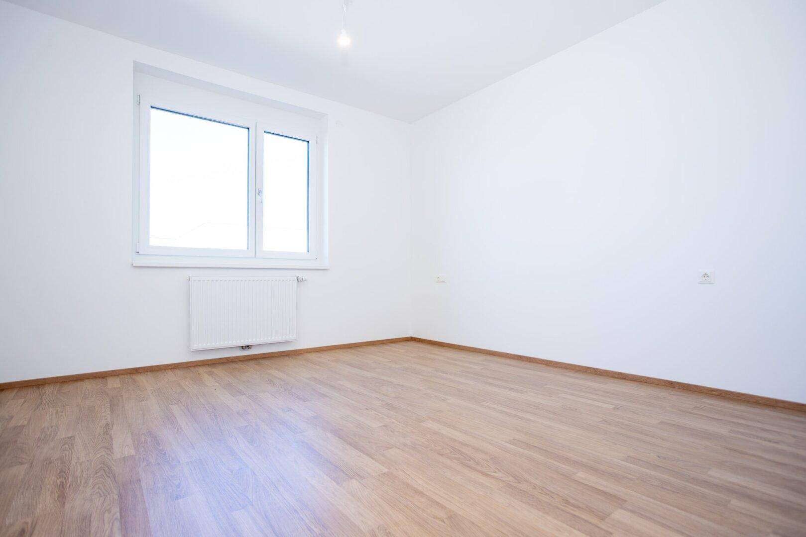Ruhiges Schlafzimmer mit Laminatboden und einem Fenster, das viel Tageslicht hereinlässt.