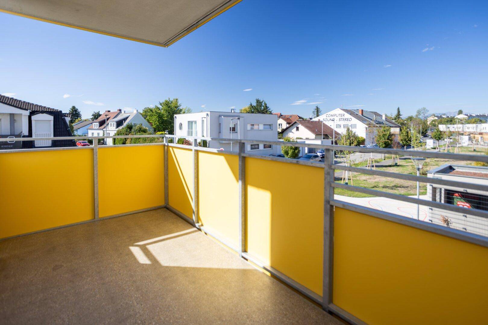 Sonniger Balkon mit gelben Brüstungselementen und Blick auf die umliegende Wohngegend.