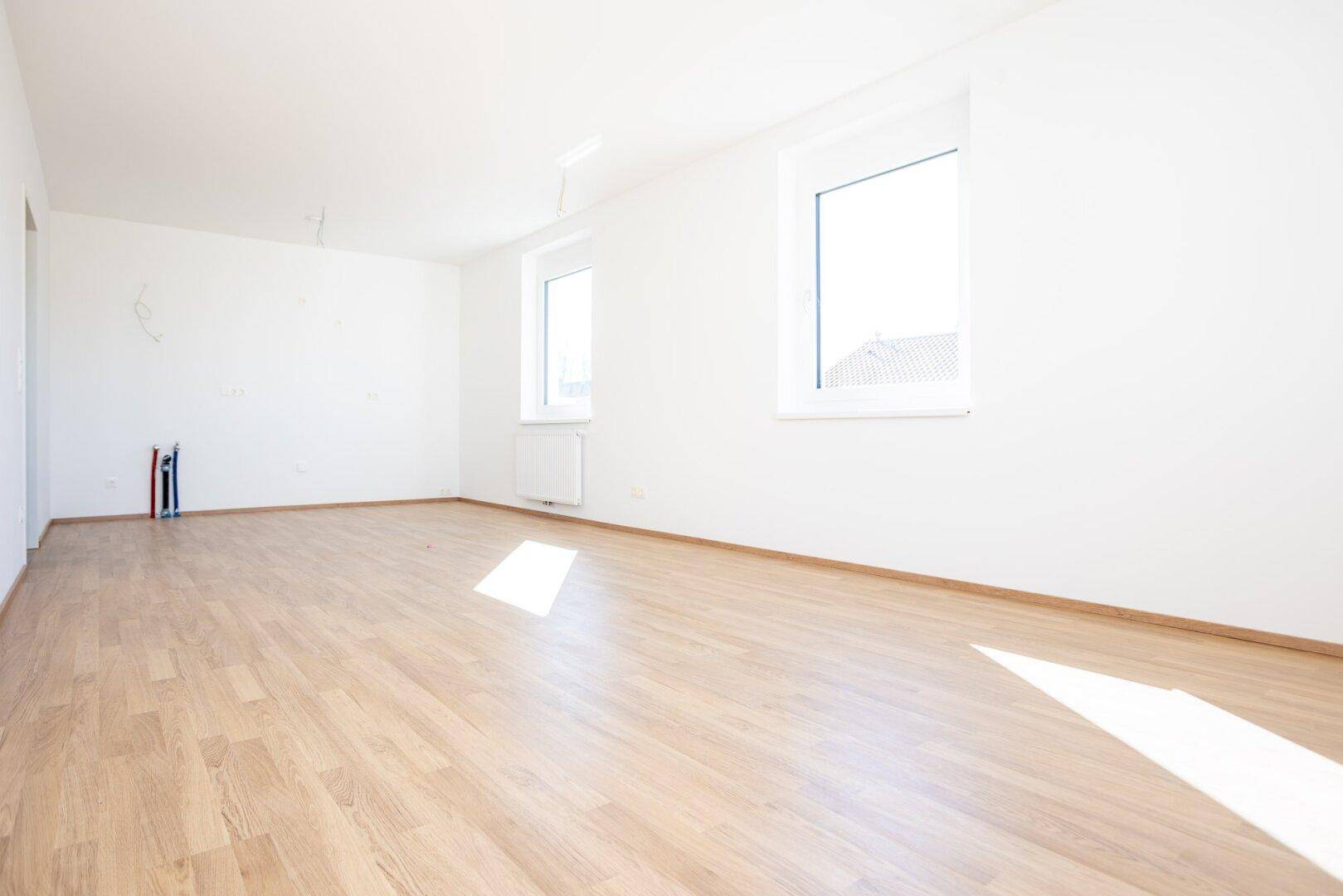 Leerer Küchenbereich mit Laminatboden und großen Fenstern, ideal für eine moderne Einbauküche.