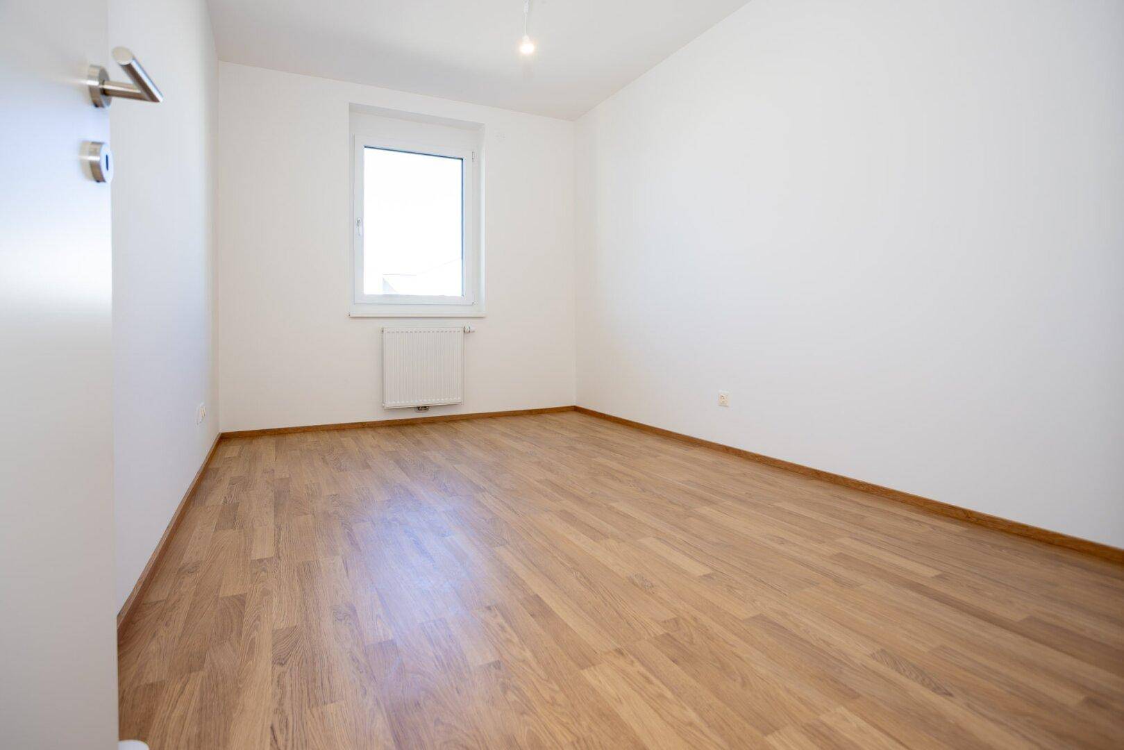 Leeres Zimmer mit Laminatboden und weiß gestrichenen Wänden, bereit für neue Bewohner.