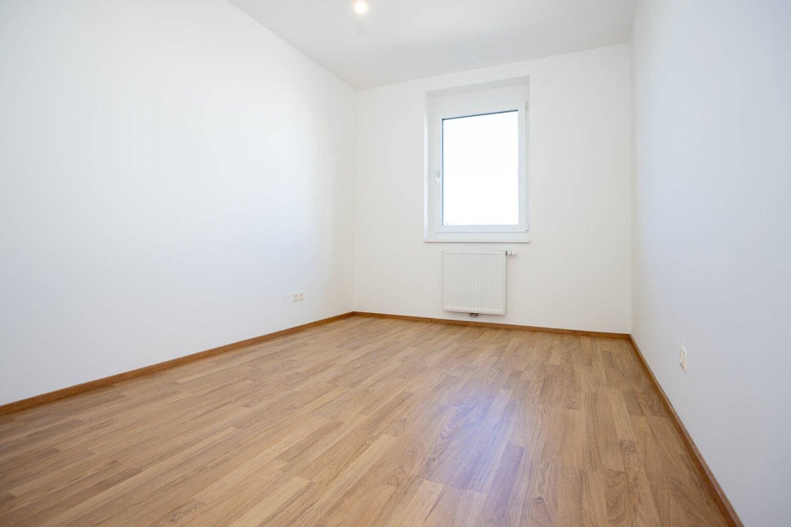 Freundliches Zimmer mit Laminatboden und einem Fenster, das den Raum mit Licht erfüllt.