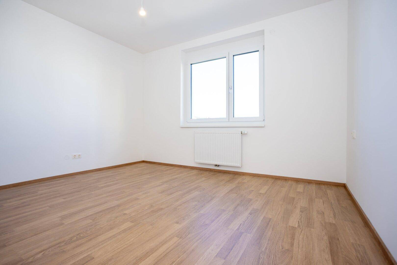 Gemütliches Zimmer mit Laminatboden und einem großen Fenster, das für eine angenehme Atmosphäre sorgt.