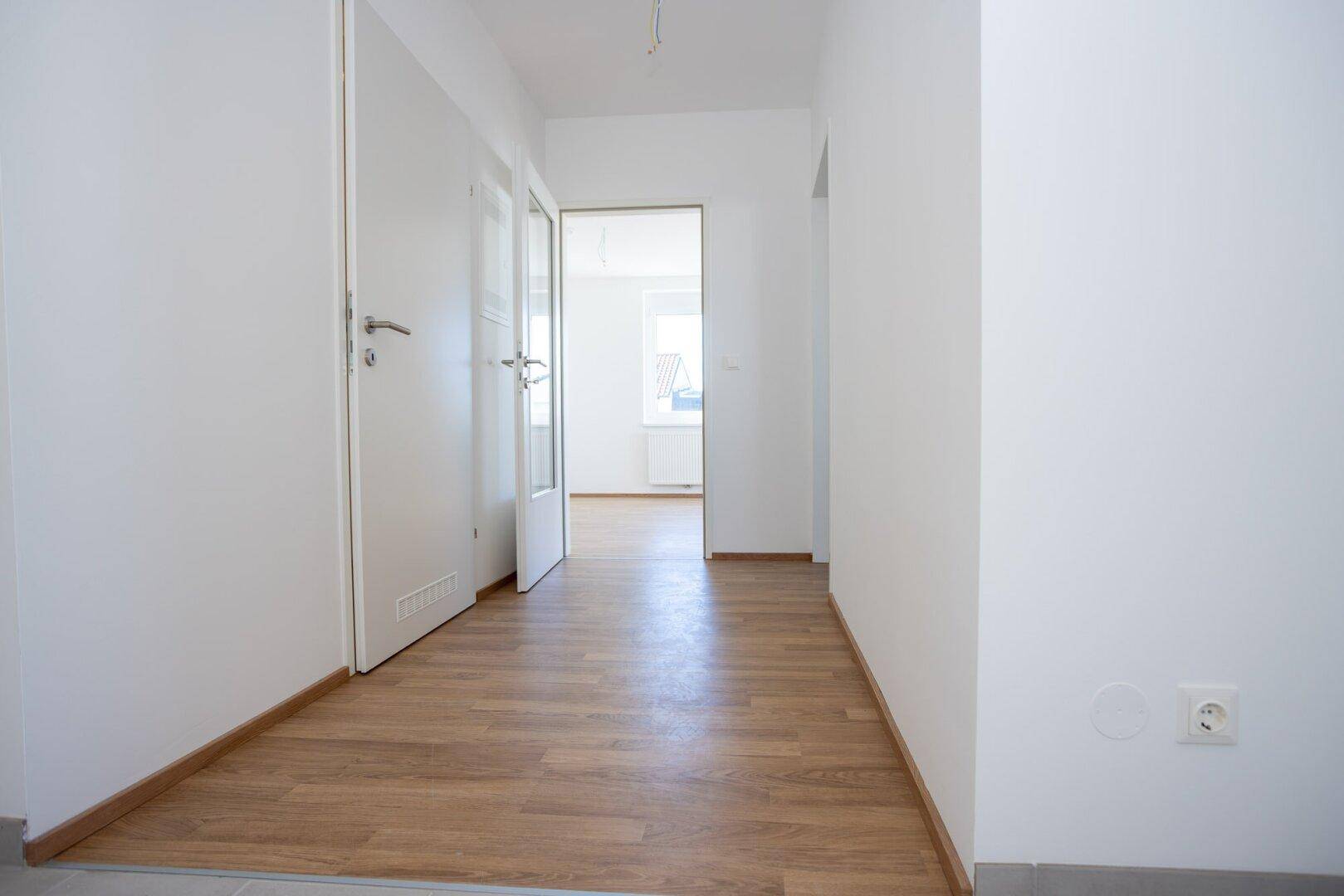 Heller Flur mit Laminat- und Fliesenboden, der zu verschiedenen Räumen führt.