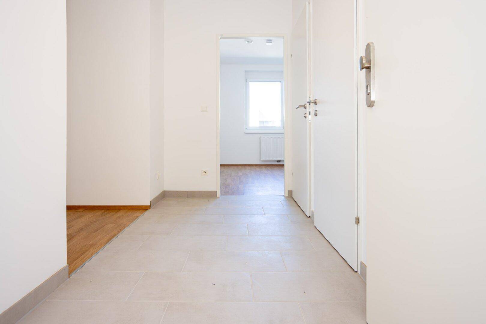 Eingangsbereich mit Fliesenboden und Übergang zu Laminat, der zu den Wohnräumen führt.