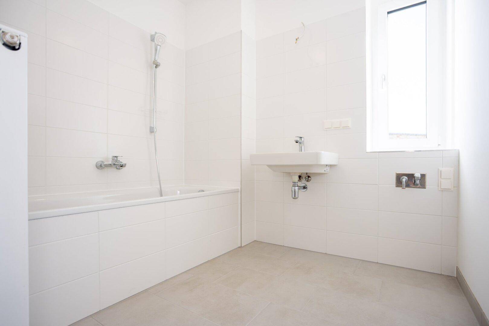 Modernes Badezimmer mit Badewanne, integrierter Dusche, Waschbecken und einem Fenster für Tageslicht.