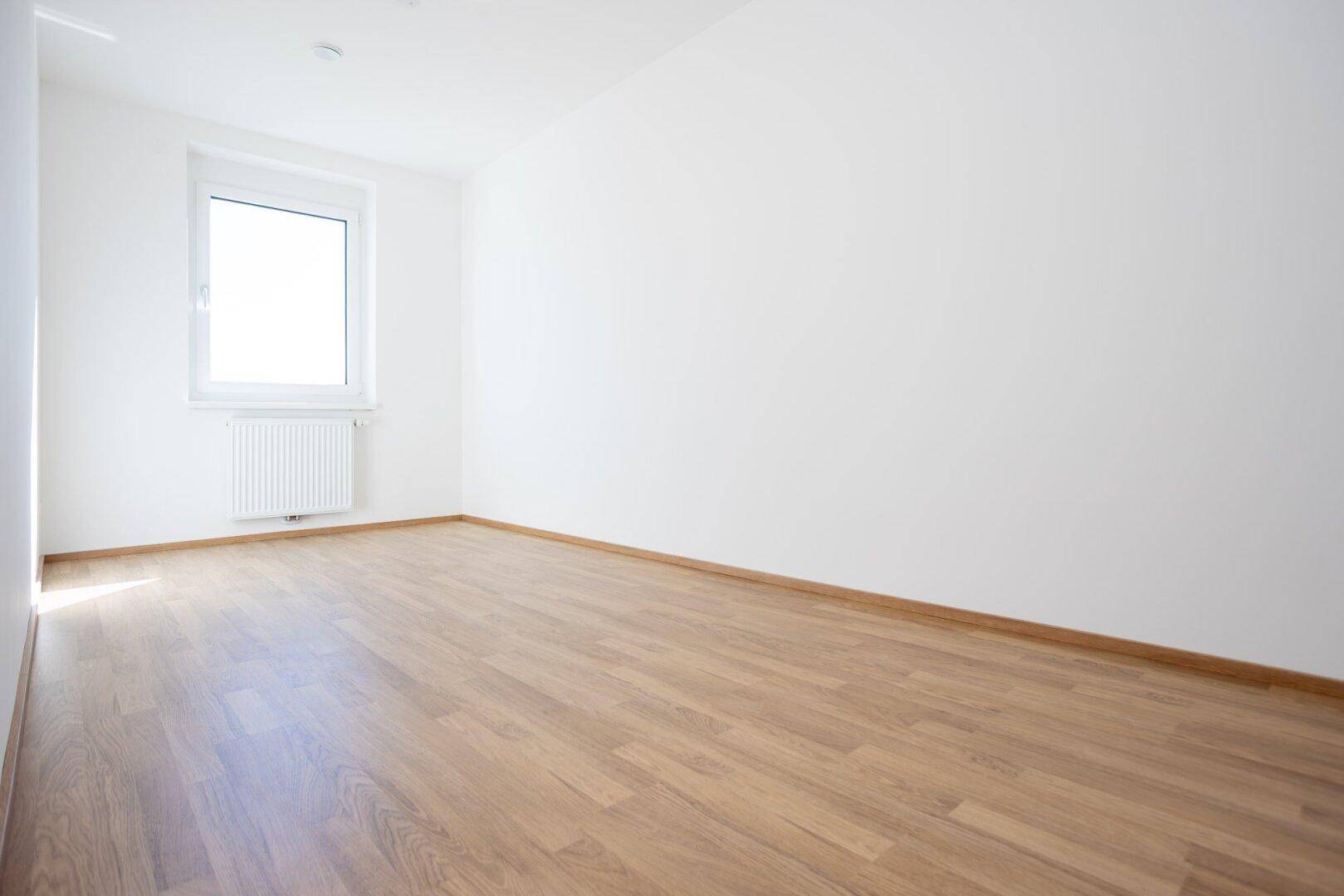 Ruhiges, helles Zimmer mit Laminatboden und einem Fenster, ideal als Schlaf- oder Arbeitszimmer.